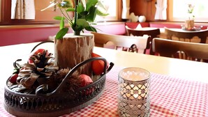 Un coin repas avec une table dressée pour deux personnes, agrémenté d’un vase de fleurs, d’un panier décoratif et d’un chandelier.