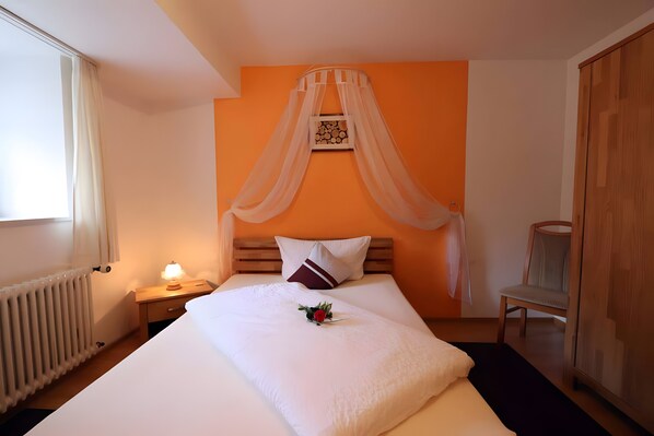 Un lit bien fait, avec une couette blanche et une fleur décorative, une table de chevet avec une lampe, une tête de lit en bois et une fenêtre avec des rideaux.