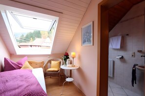 A bedroom with a skylight, a bed with purple bedding, a chair, a small table with a lamp, and a bathroom with a towel rack. - Gasthaus zur Linde – 'Sternenblick' Single Room with Shared Terrace, Garden and Wi-Fi (Oberharmersbach)