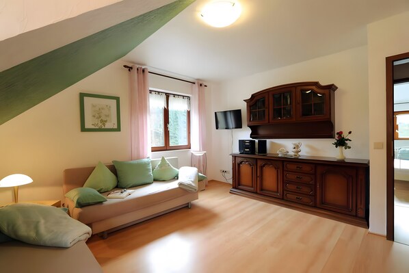 A room with a sofa, a cabinet, a flat-screen TV, and a window with curtains. - Gasthaus zur Linde – Apartment 'Tannenblick' with Shared Terrace, Garden and Wi-Fi (Oberharmersbach)