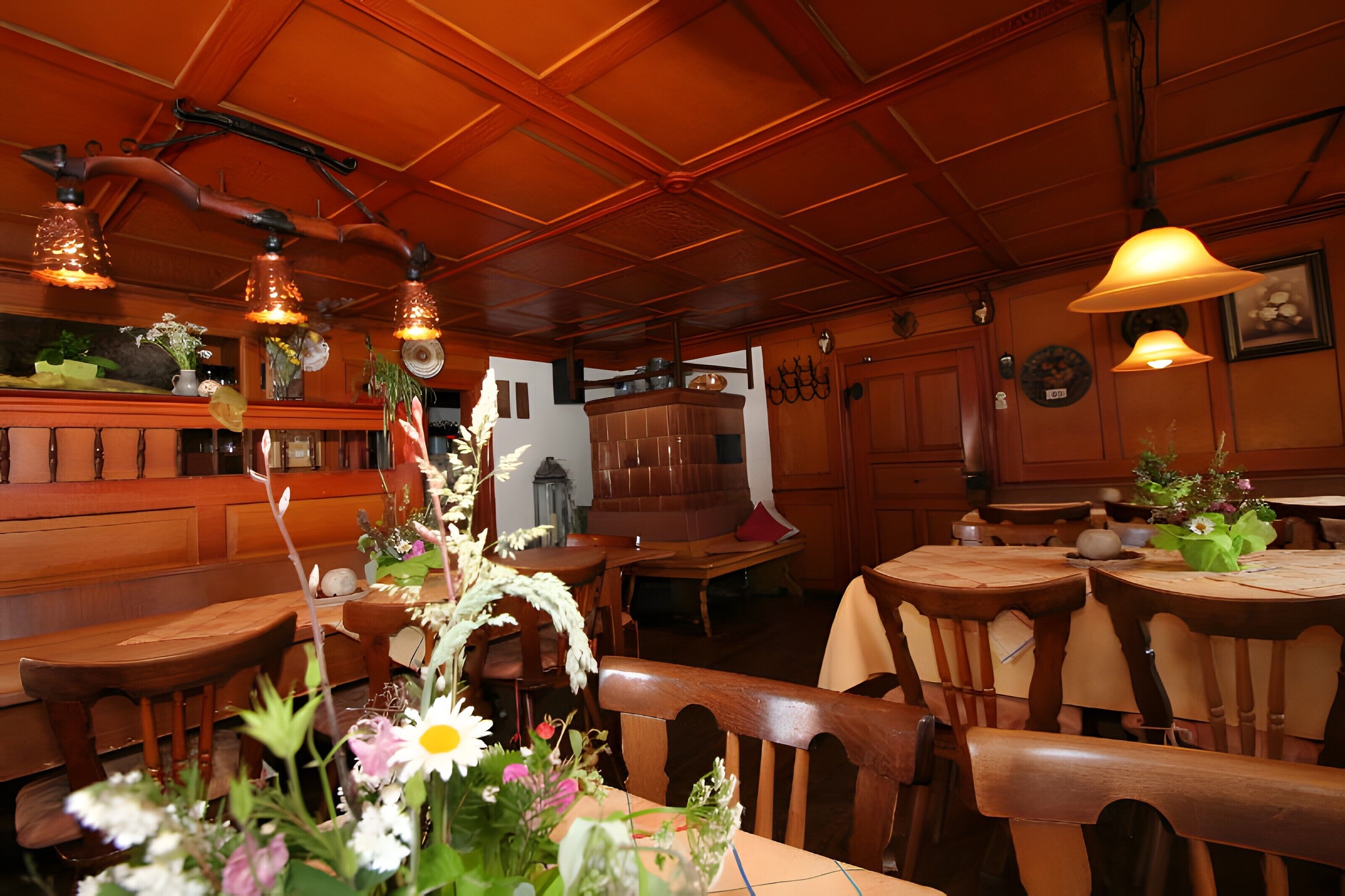 L’intérieur d’un restaurant, avec des meubles en bois, des luminaires suspendus et des compositions florales en guise de décoration centrale.