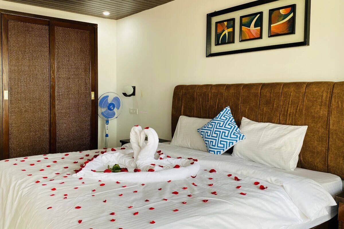 A hotel room with a bed adorned with rose petals and a swan-shaped towel arrangement.