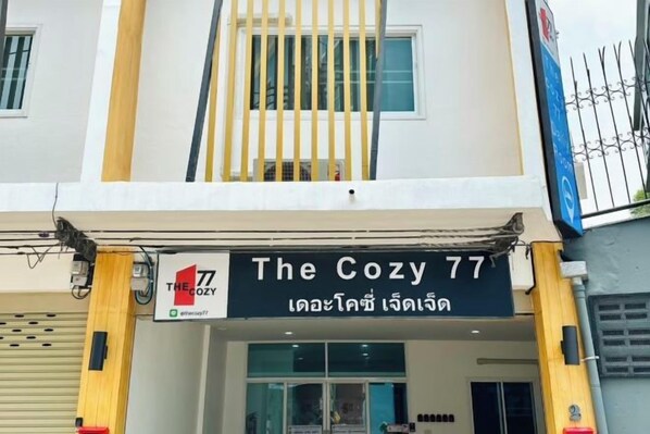 A building with a sign reading 'The Cozy 77' and a Thai phrase below it.