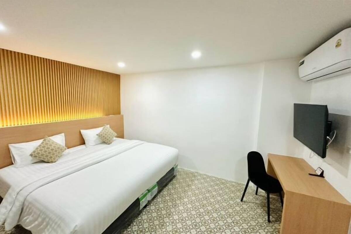 A hotel room with a bed, a desk, a chair, a TV, and an air conditioner.