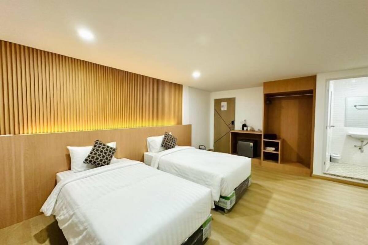 A hotel room with two beds, a wooden headboard, a desk, and a bathroom with a shower.
