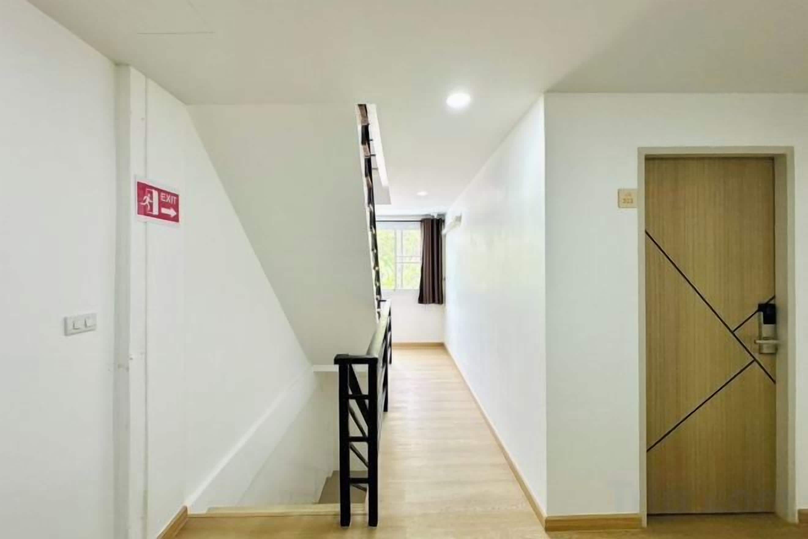 A hallway with a staircase, a wooden door, and a red emergency exit sign.