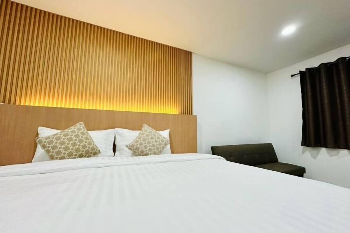 A hotel room with a bed, a headboard, a sofa, and a curtain.