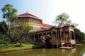 A large building with a red roof, a pavilion with a roof, and a body of water in front.