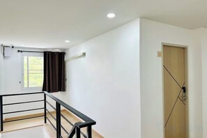 A room with a wooden door, a window with curtains, and a staircase with a black railing. - The Cozy77 – No Parking (Bangkok)