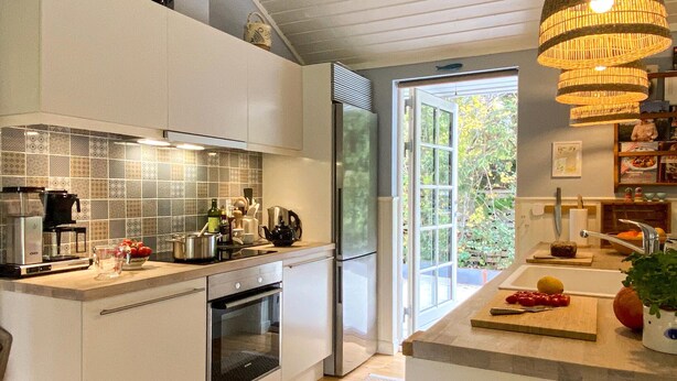 Een moderne keuken met witte kastjes, een inbouwoven, een koffiezetapparaat en een groot raam met uitzicht op groen.