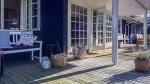 Een overdekt houten terras met een bank en rieten manden.