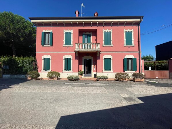 A two-story building with a balcony, a red facade, and green shutters.