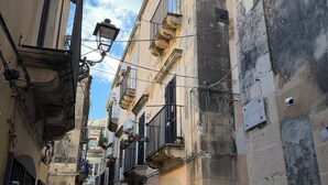 A narrow street with historic buildings, stone pavement, and balconies with potted plants. - A stone's throw from the cathedral: authentic Sicilian house in Ortigia (Siracusa)