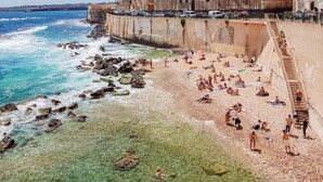 A coastal beach with clear waters, rocky shore, and historic buildings. - A stone's throw from the cathedral: authentic Sicilian house in Ortigia (Siracusa)