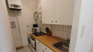 Cocina compacta con armarios blancos, encimera de madera, horno integrado, lavadora y un lavamanos.
