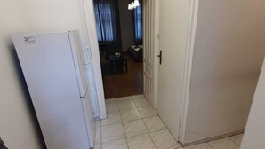 Un estrecho pasillo con suelo de baldosas que conduce a una sala de estar con sofá y cortinas.