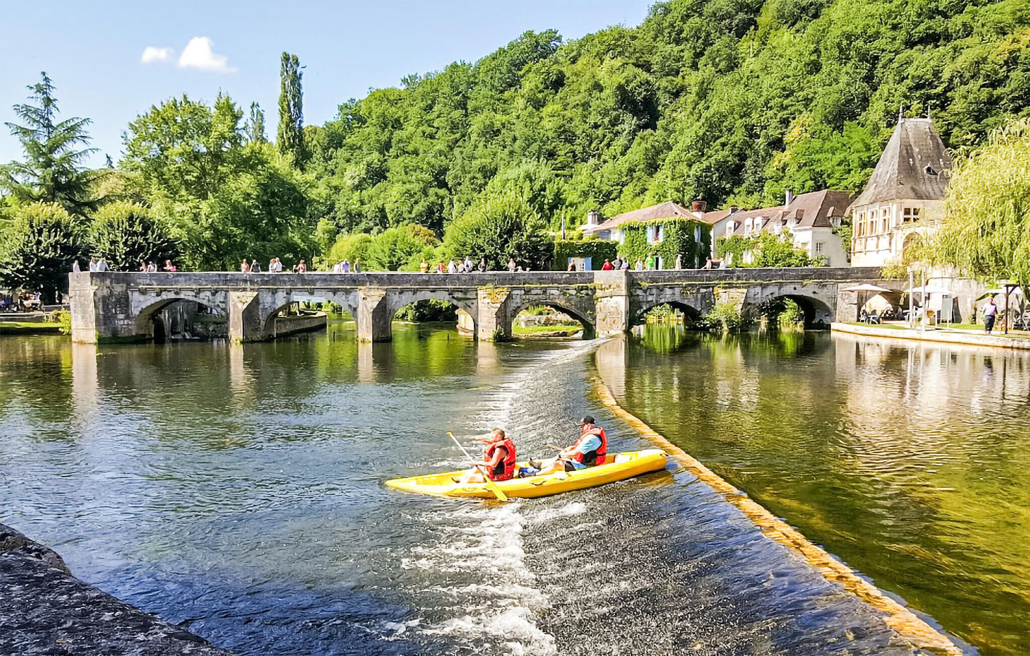 A river with a bridge and a yellow boat with two people paddling.