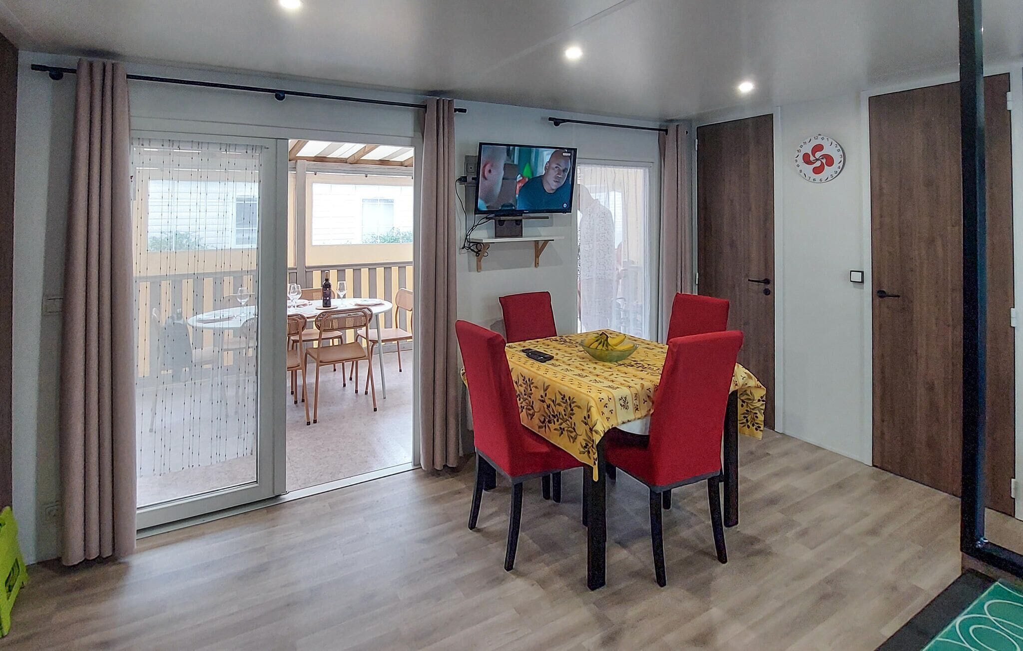A dining area with a table set for four, red chairs, and a television mounted on the wall.