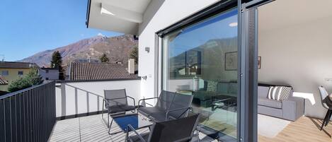 Een modern balkon met een glazen deur, een bank en een eettafel.