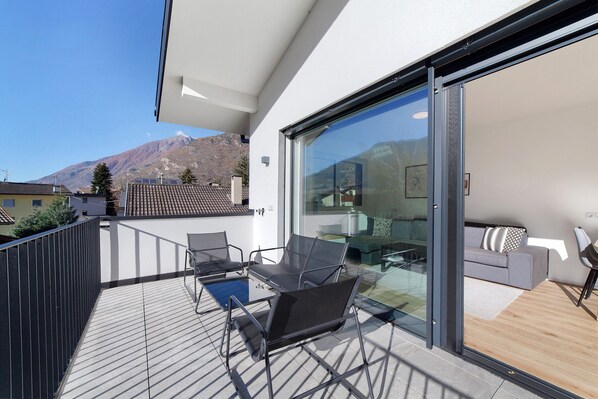 A modern balcony with a glass door, a sofa, and a dining table.