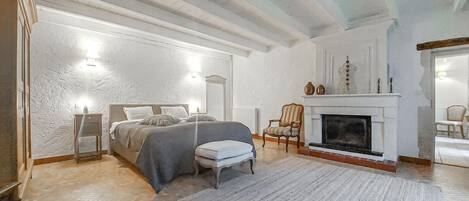 A bedroom with a bed, a chair, a fireplace, and a nightstand.