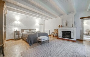 A bedroom with a bed, a chair, a fireplace, and a nightstand.