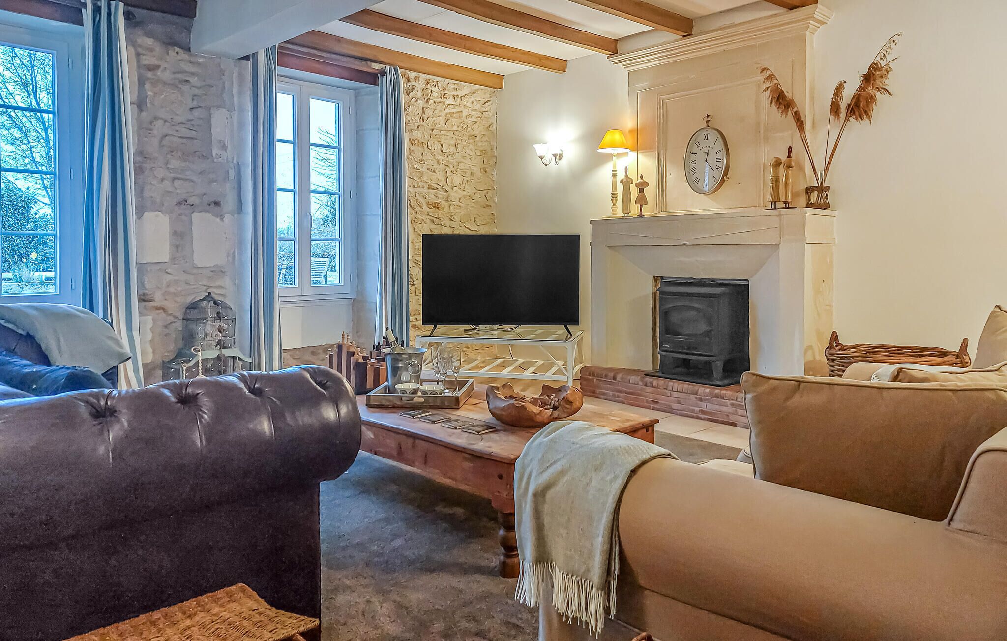 A cozy living room with a stone wall, a fireplace, a television, and leather sofas.