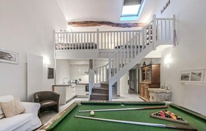 A spacious living area with a pool table, a high ceiling with exposed beams, a staircase to an upper level, and a cozy seating area.