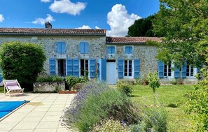 A stone building with blue shutters, a pool, and a garden with lavender.