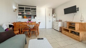 Un espacio habitable compacto con comedor, kitchenette y televisor montado en la pared.