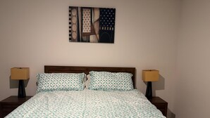 Ein ordentlich bezogenes Bett mit gemusterten Betttextilien, zwei Nachttischlampen und einem Bild über dem Bett.