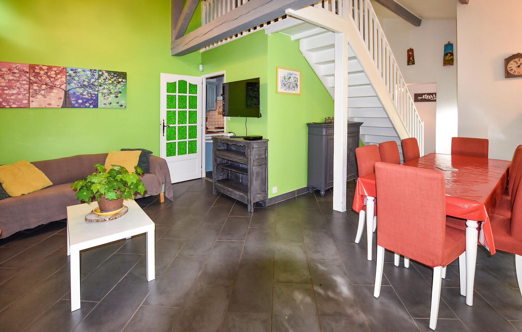 Een woonkamer met een groene muur, een witte trap, een eethoek met rode stoelen en een grijze kast.