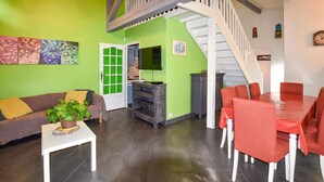 A living room with a green wall, a white staircase, a dining area with red chairs, and a grey cabinet.