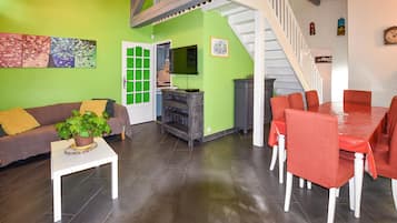 Een woonkamer met een groene muur, een witte trap, een eethoek met rode stoelen en een grijze kast.