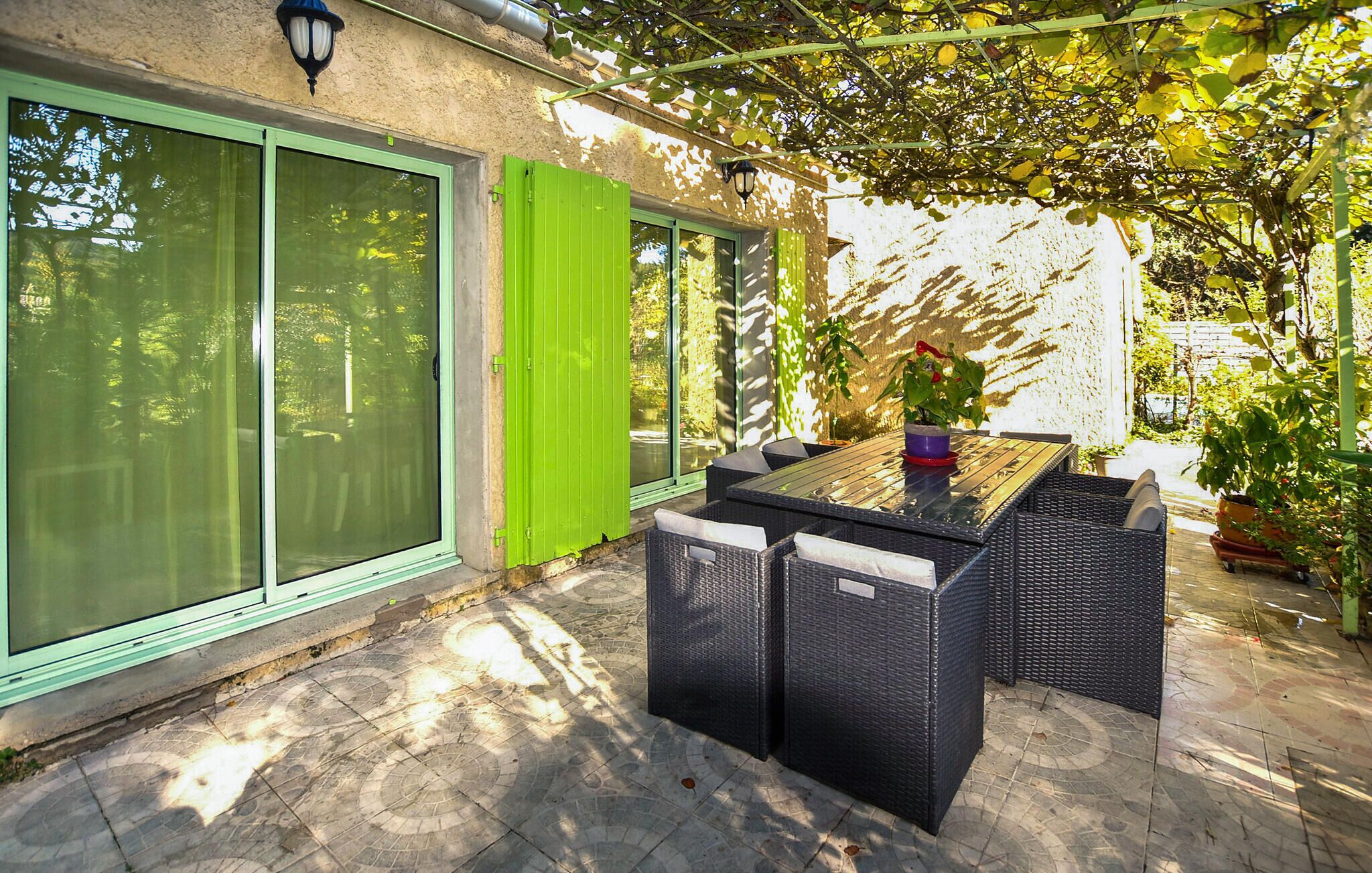 Une terrasse extérieure avec une table et des chaises, une porte verte et une pergola couverte de plantes grimpantes.