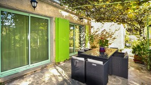 An outdoor patio with a table and chairs, a green door, and a pergola with climbing plants.