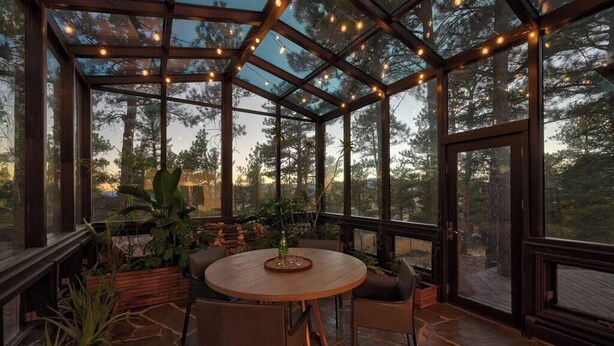 A conservatory with a glass ceiling, wooden furniture, and potted plants.