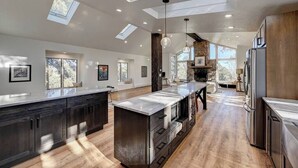 A spacious kitchen with a large island, skylights, and a stone fireplace.