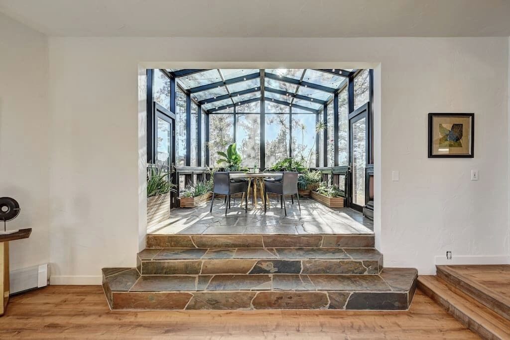 Een modern interieur met een stenen trap die leidt naar een glazen patio met buitenmeubilair en planten.