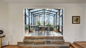 A modern interior with a stone staircase leading to a glass-enclosed patio area with outdoor furniture and plants.