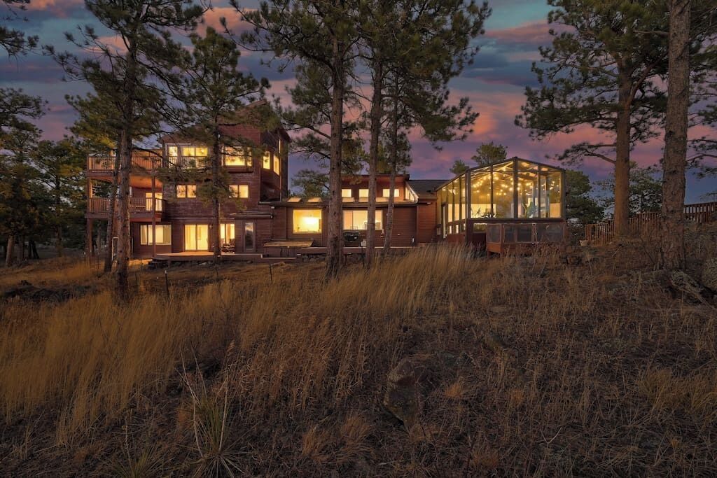 Een modern gebouw met twee verdiepingen, grote ramen en een glazen constructie, omringd door hoge bomen en grasvelden.