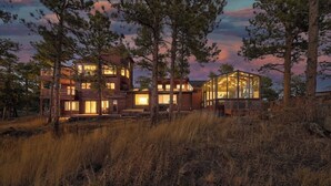 A modern two-story building with large windows and a glass structure, surrounded by tall trees and grassy terrain.