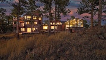 Een modern gebouw met twee verdiepingen, grote ramen en een glazen constructie, omringd door hoge bomen en grasvelden.