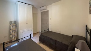 A bedroom with two single beds, a wardrobe, a radiator, and an air conditioning unit.