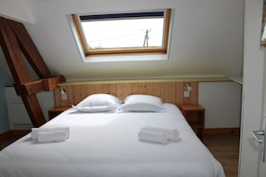 A bedroom with a skylight, wooden headboard, two bedside tables, and a neatly made bed with towels. - Comfortable 2** gîte 5 min from the beach, 10 min from Pointe du Hoc, 20 min from Omaha (Grandcamp-Maisy)