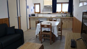En kompakt opholdsstue med spisebord, stole, sofa, fjernsyn og et tekøkken med mikrobølgeovn og kaffemaskine.