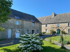 A stone building with a green door, a bench, and a white flowering bush. - Comfortable 2** gîte 5 min from the beach, 10 min from Pointe du Hoc, 20 min from Omaha (Grandcamp-Maisy)