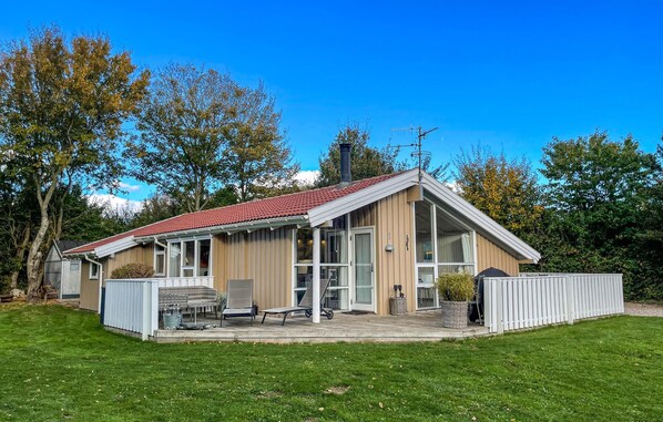 A single-story house with a red-tiled roof, a covered patio with outdoor furniture, and a fenced yard.