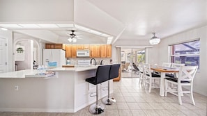 Een moderne keuken met een centraal eiland, houten kastjes en een eethoek met witte stoelen.
