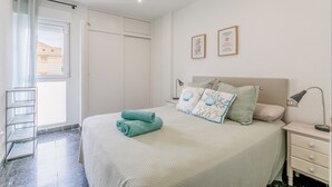 A bedroom with a bed, a nightstand, a lamp, a ceiling fan, a window with a curtain, and a door. - Apartment 'Mar 4 En Santa Pola' with Sea View, Private Terrace and Wi-Fi (Santa Pola)